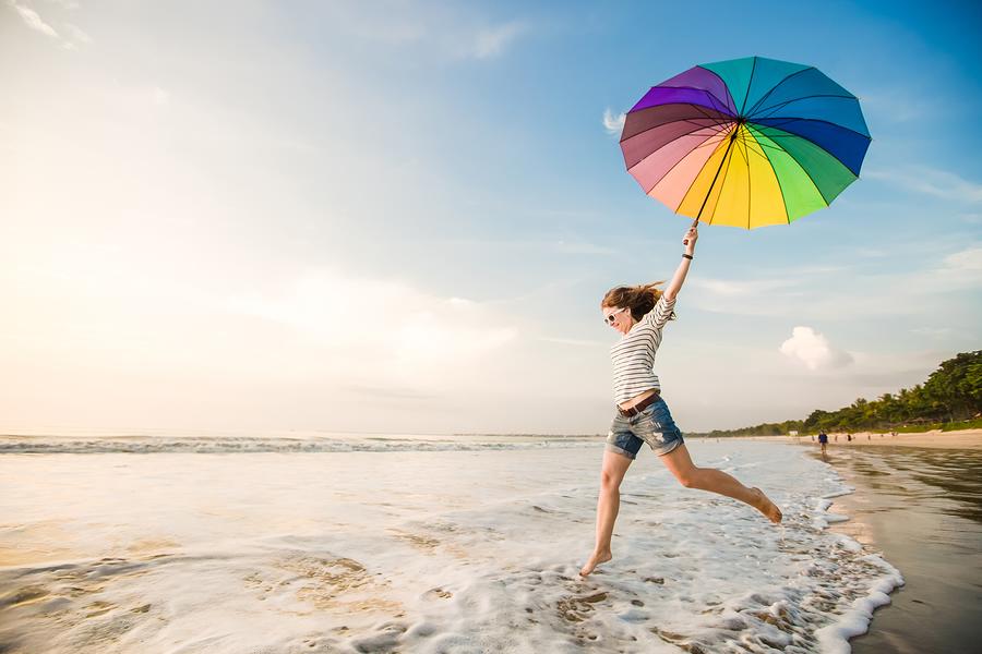 A photo of a happy woman carrying a colorful umbrella, splashing through foamy waves on the beach.