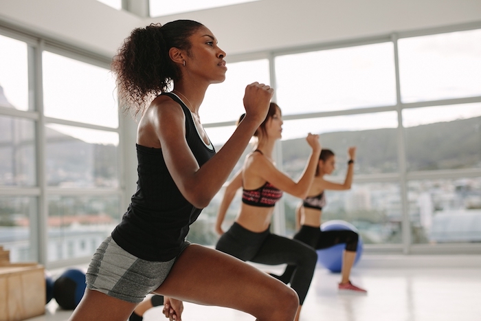 A photo of three women doing walking lunges during a fitness class at the gym.