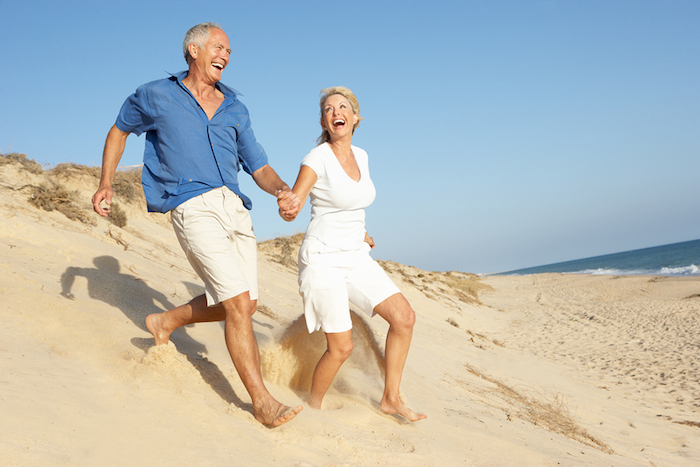 A photo of a happy, mature couple running across sand dunes by the ocean.