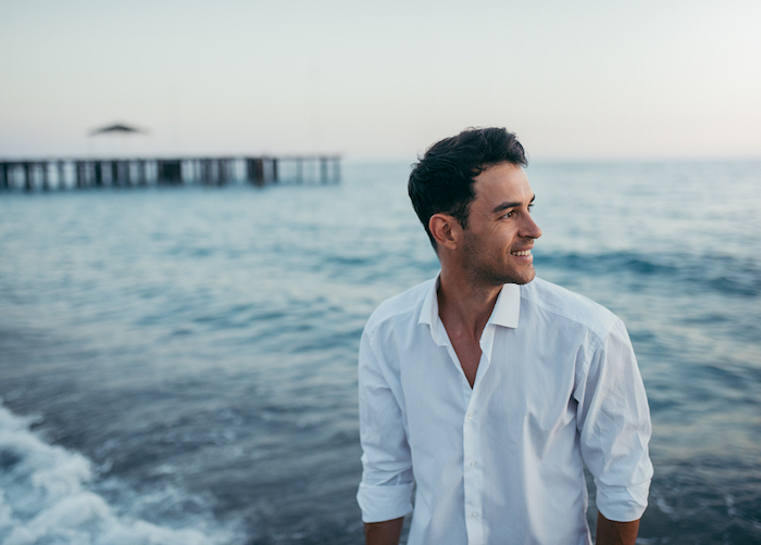 A photo of a handsome young man standing in ocean waves as the sun sets.