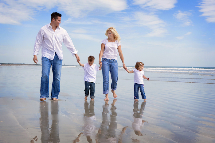 A photo of a family of four walking barefoot in shallow water on a beach.
